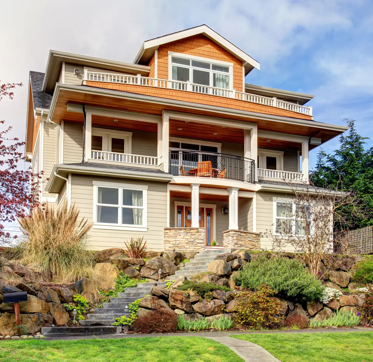 A three-story craftsman home with wraparound balconies on a landscaped hillside